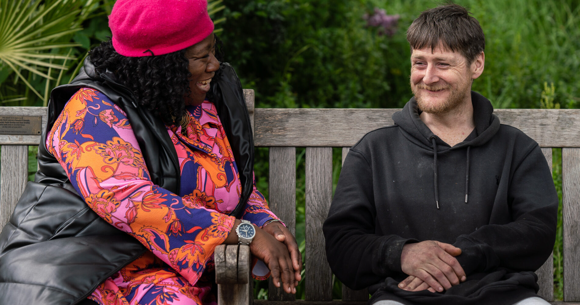 A support worker sits on a park bench and chats with a Look Ahead customer who has experienced homelessness.