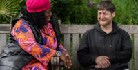 A support worker sits on a park bench and chats with a Look Ahead customer who has experienced homelessness.