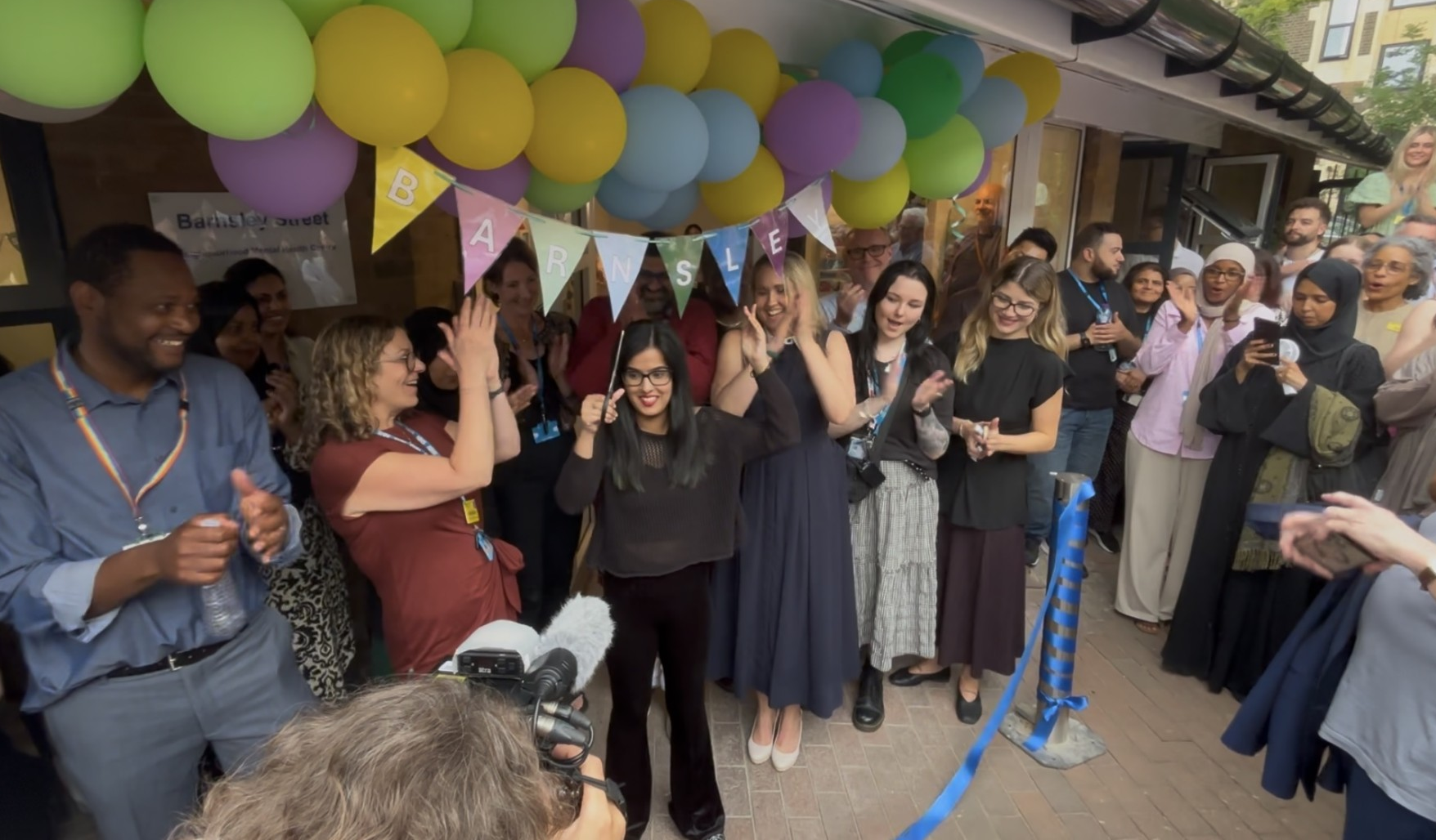 A group of staff from Look Ahead, the East London NHS Foundation Trust and other local partners celebrate the opening of the Barnsley Street Project by cutting a ribbon outside the building.