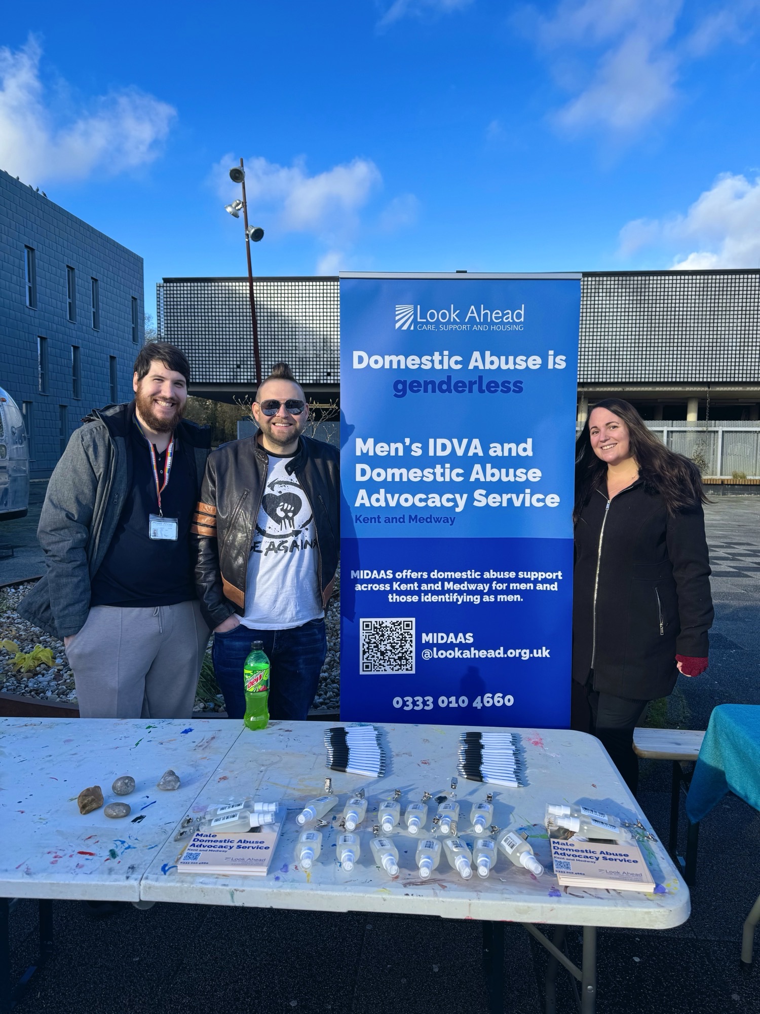 3) Three staff from Look Ahead's MIDAAS service standing at a stall with information on men's experience of domestic abuse at Kent University.