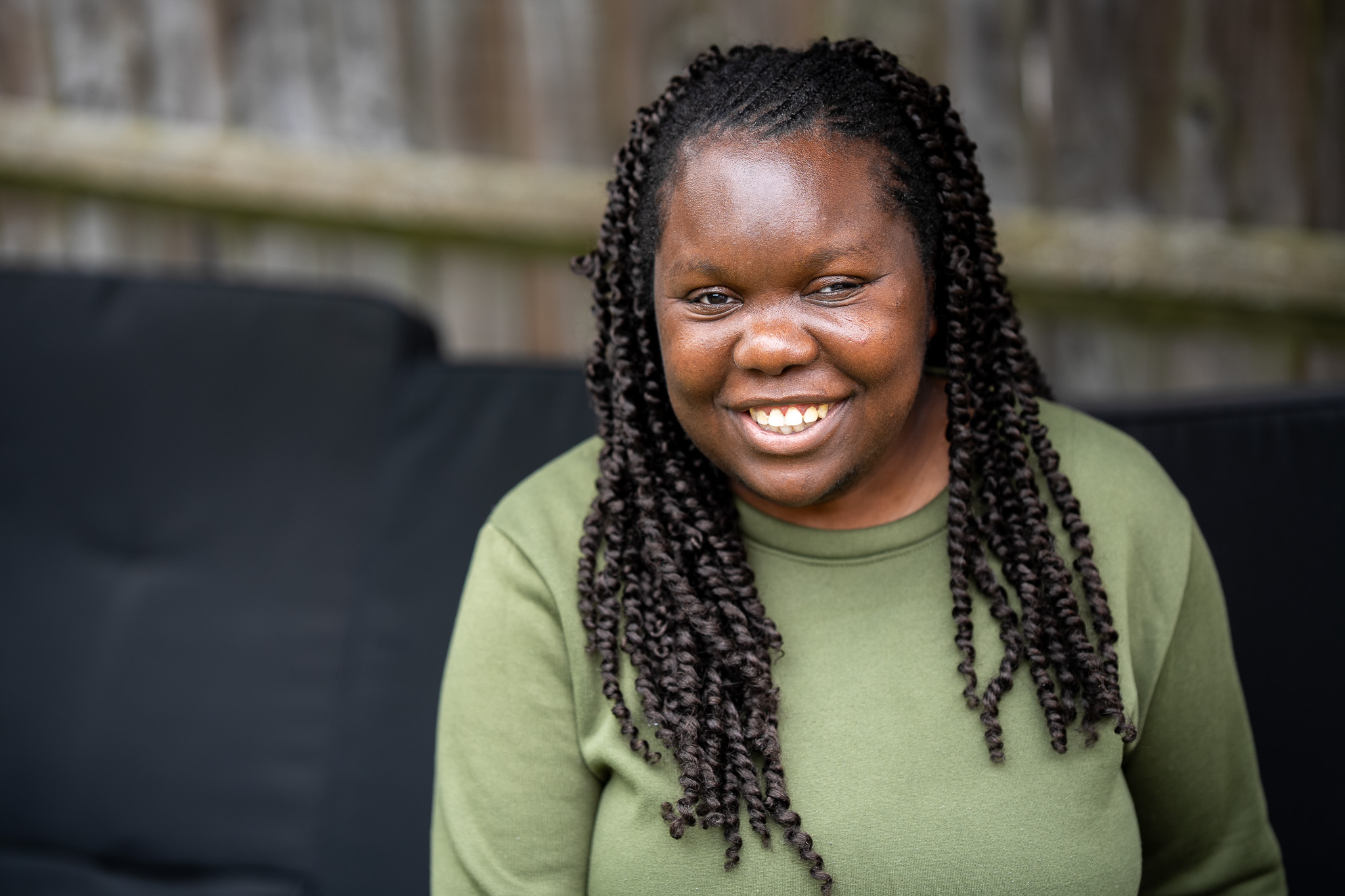 A smiling woman in a khaki green top with braided hair.