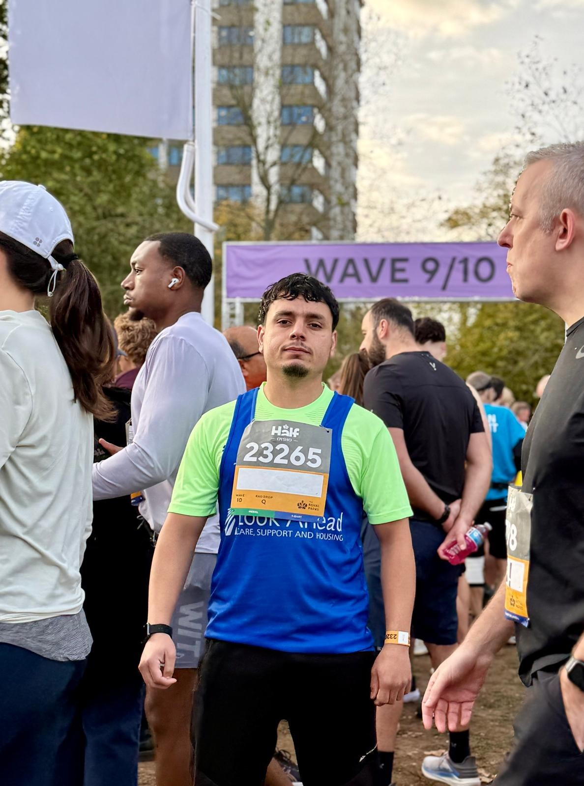 A young man in a bright green t-shirt and blue Look Ahead runners' vest in front of a group of other runners.