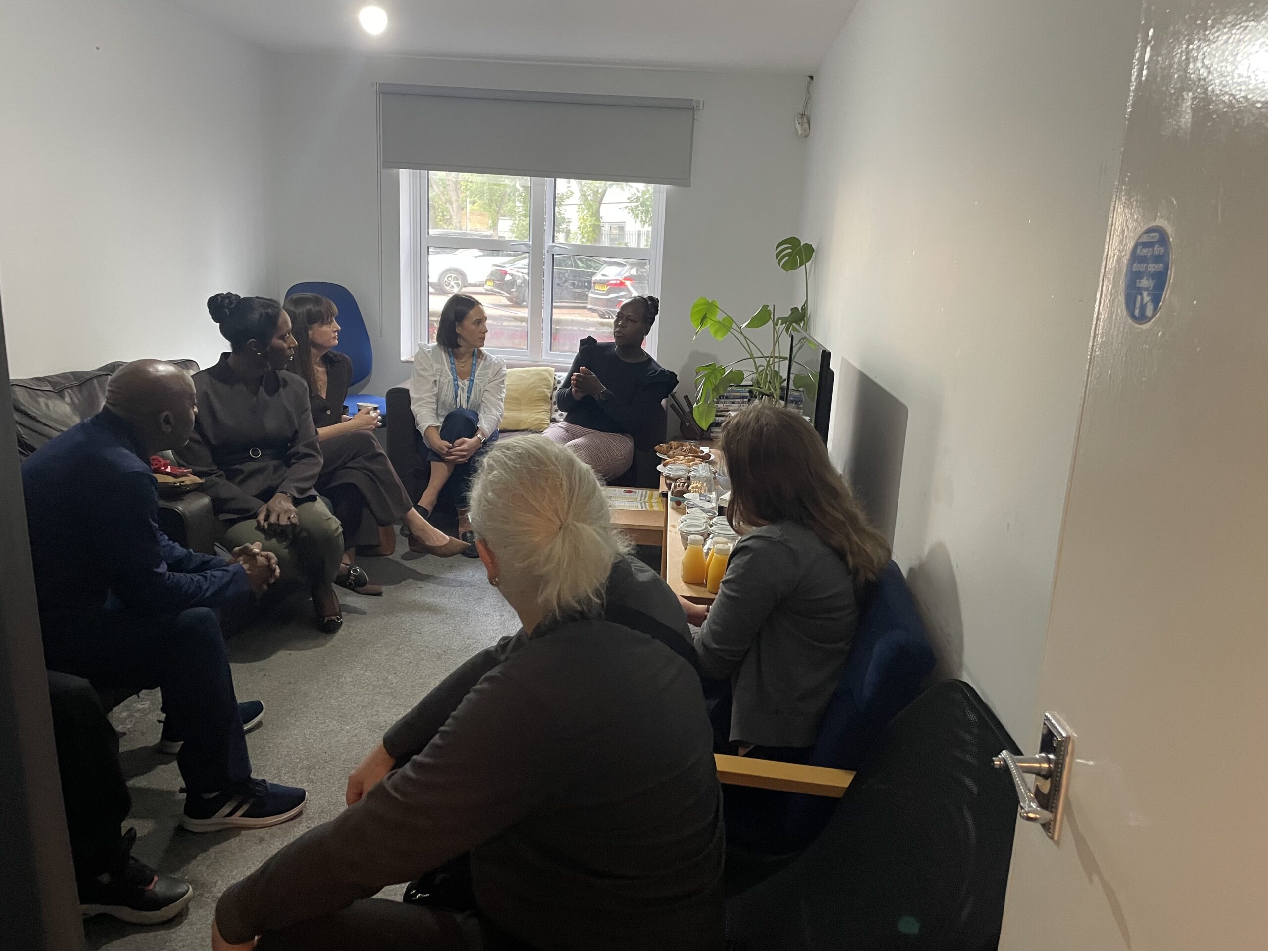A group of people sitting and talking in a lounge with juice and pastries on a table.
