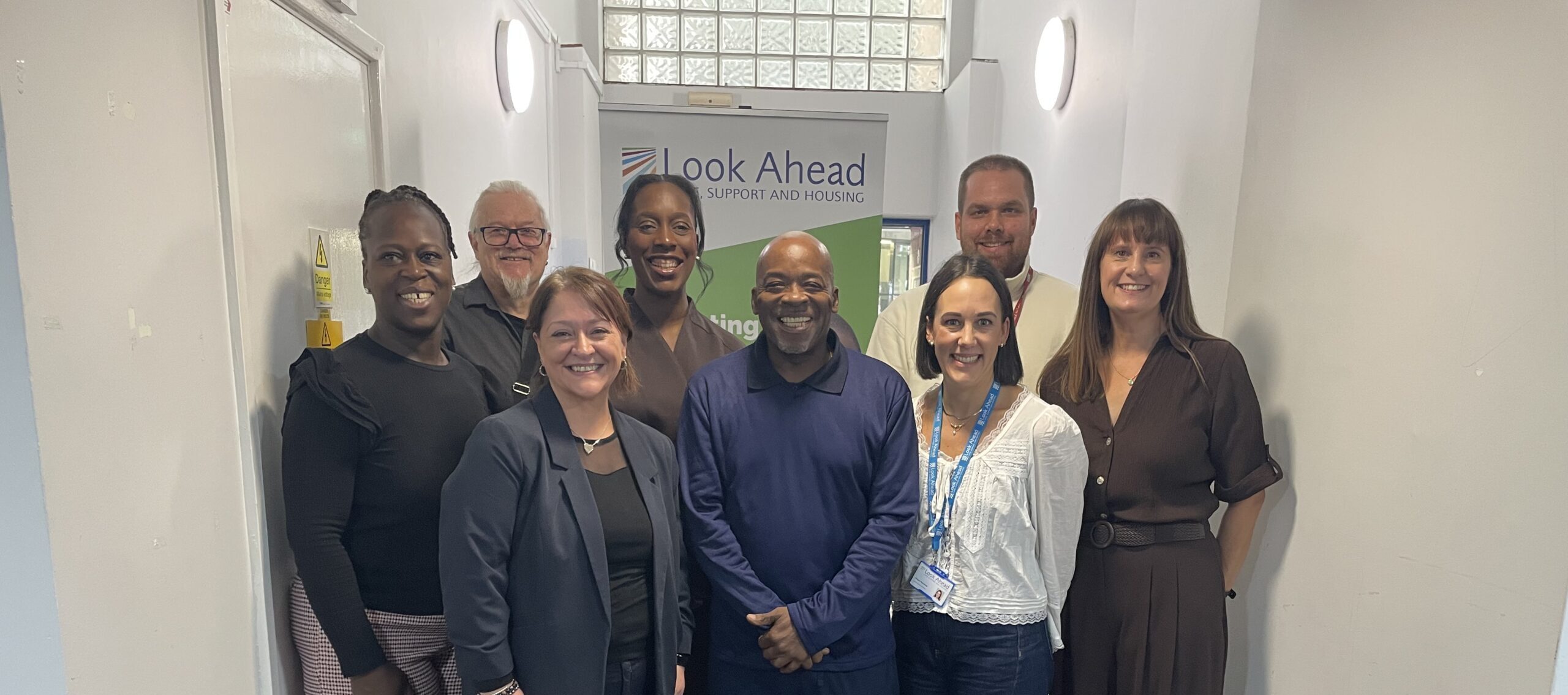A group of smartly dressed people standing and smiling in front of a Look Ahead branded banner.